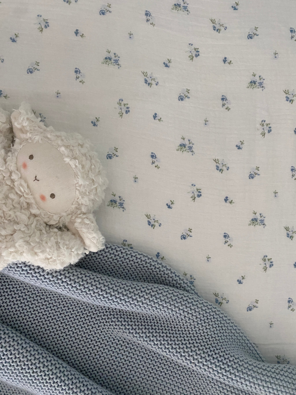 Ivory lamb comforter resting on a blue knitted baby blanket with a floral muslin backdrop.