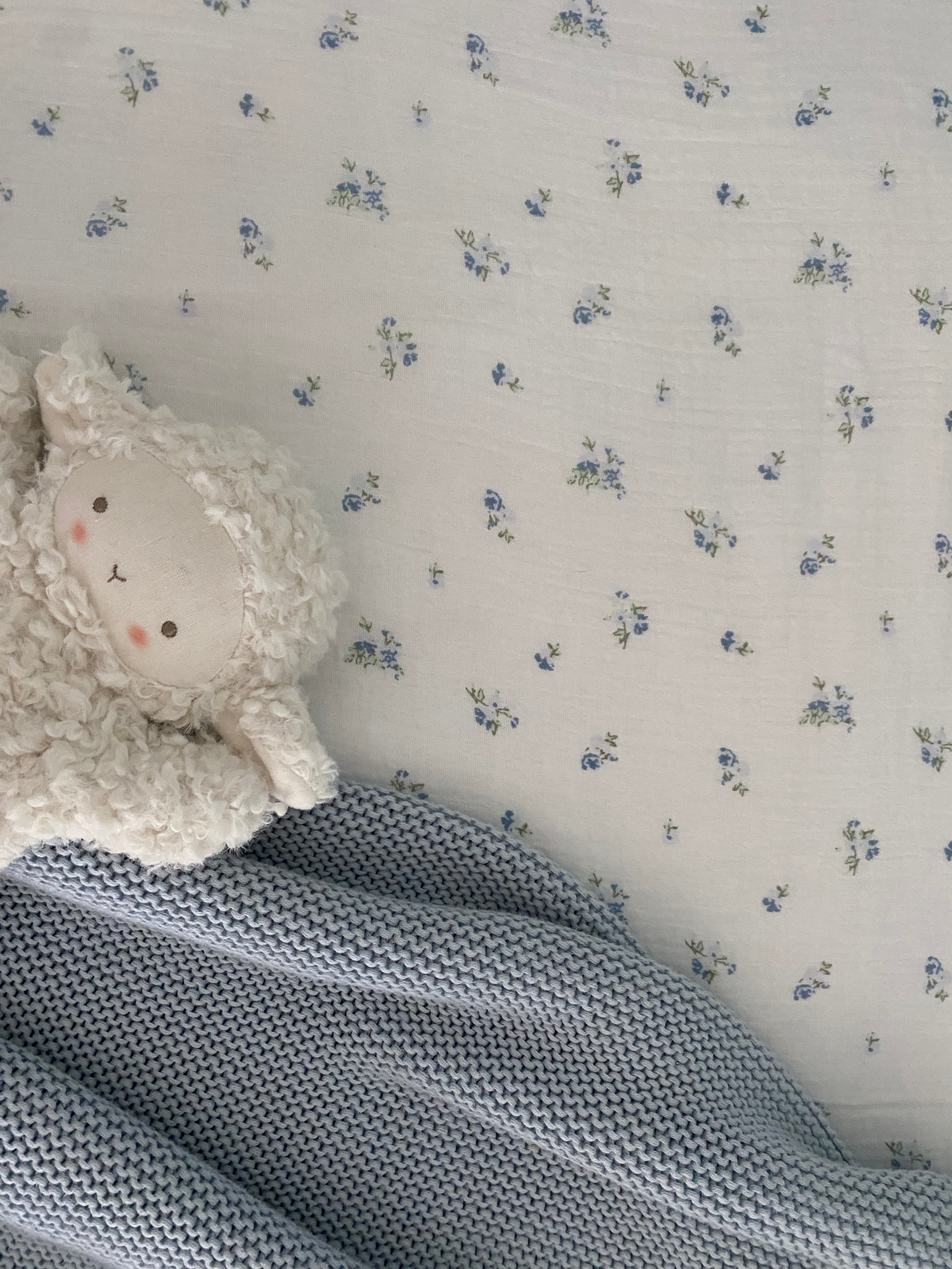Ivory lamb comforter resting on a blue knitted baby blanket with a floral muslin backdrop.